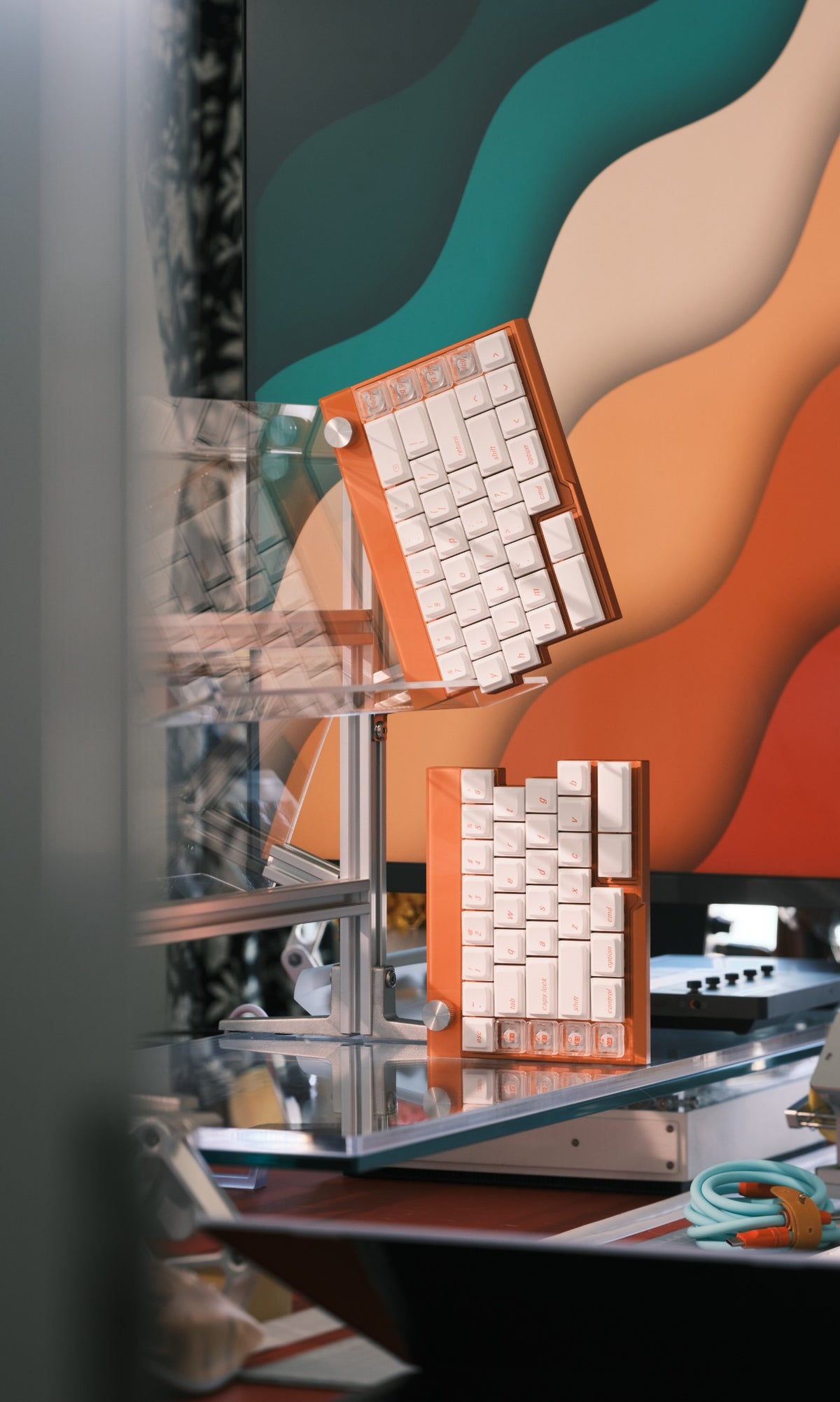 Orange Jiffy75 split keyboard with white keycaps on a display stand